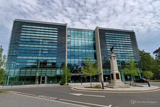 A photo of a tall building with green glass against a dappled sky