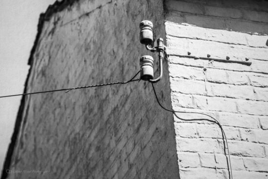 Black and white image of an old open wire telephone bracket on a white wall. 