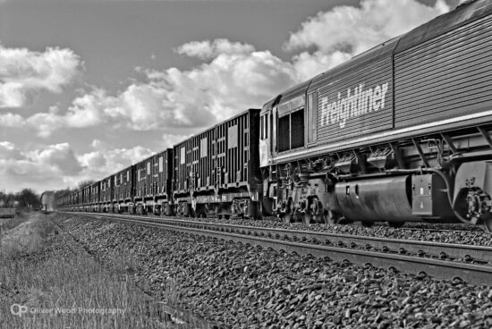 A black and white picture of a freightliner locomotive and long train of containers